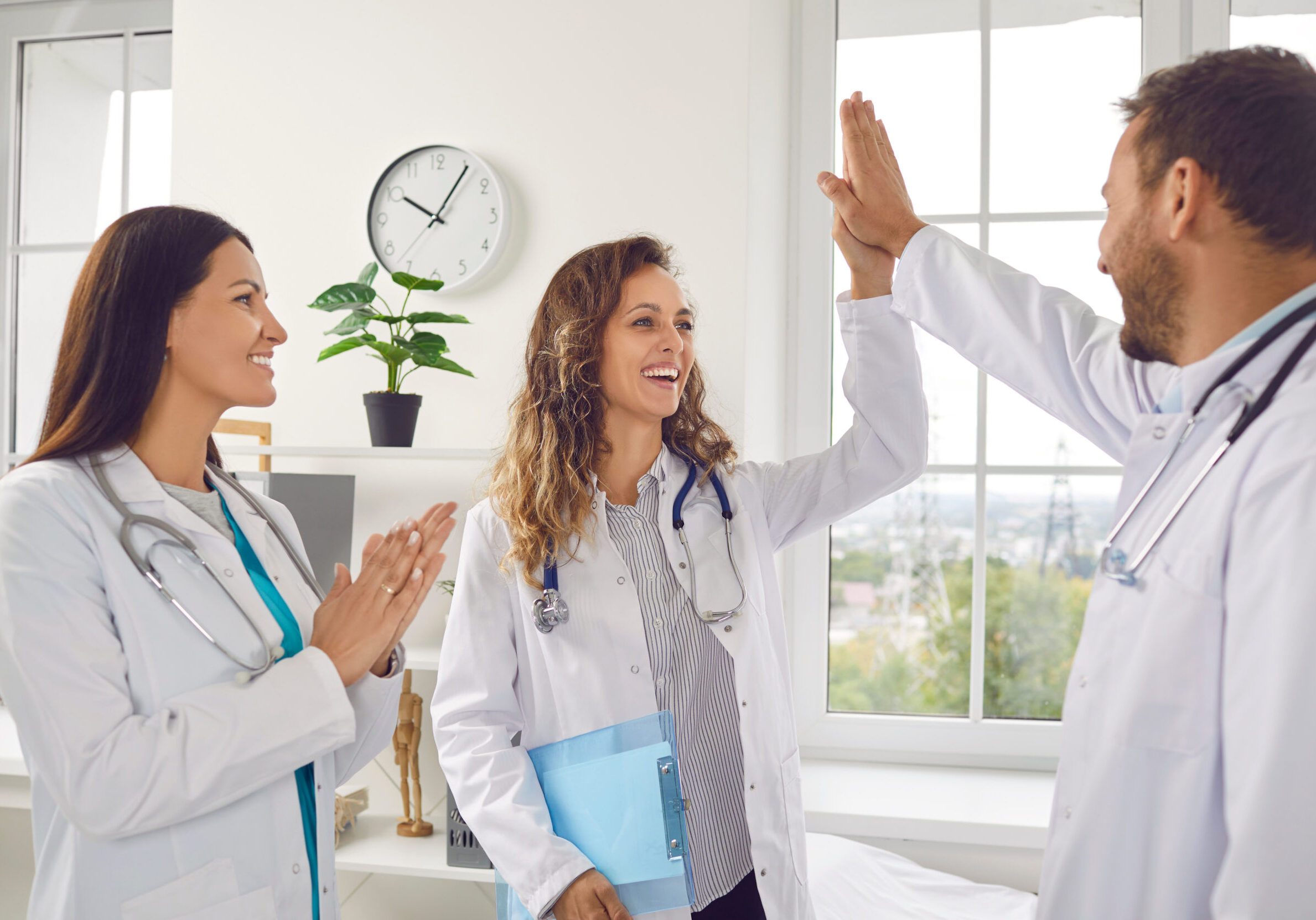 Doctors rejoicing at success in treatment giving high five each other standing in clinic Happy smiling doctors rejoicing at success in treatment giving high five each other standing in clinic. Successful team of young medical staff in white uniform in hospital. Health care concept.